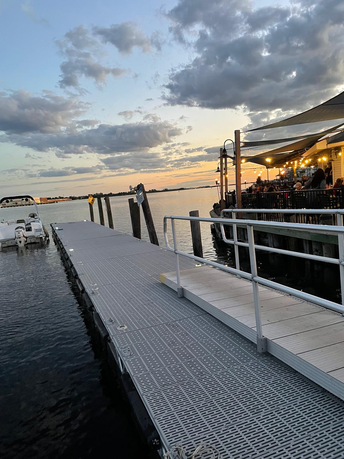 The dock at Bayhouse at sunset, with a boat tied up and diners on the lit waterfront deck beyond
